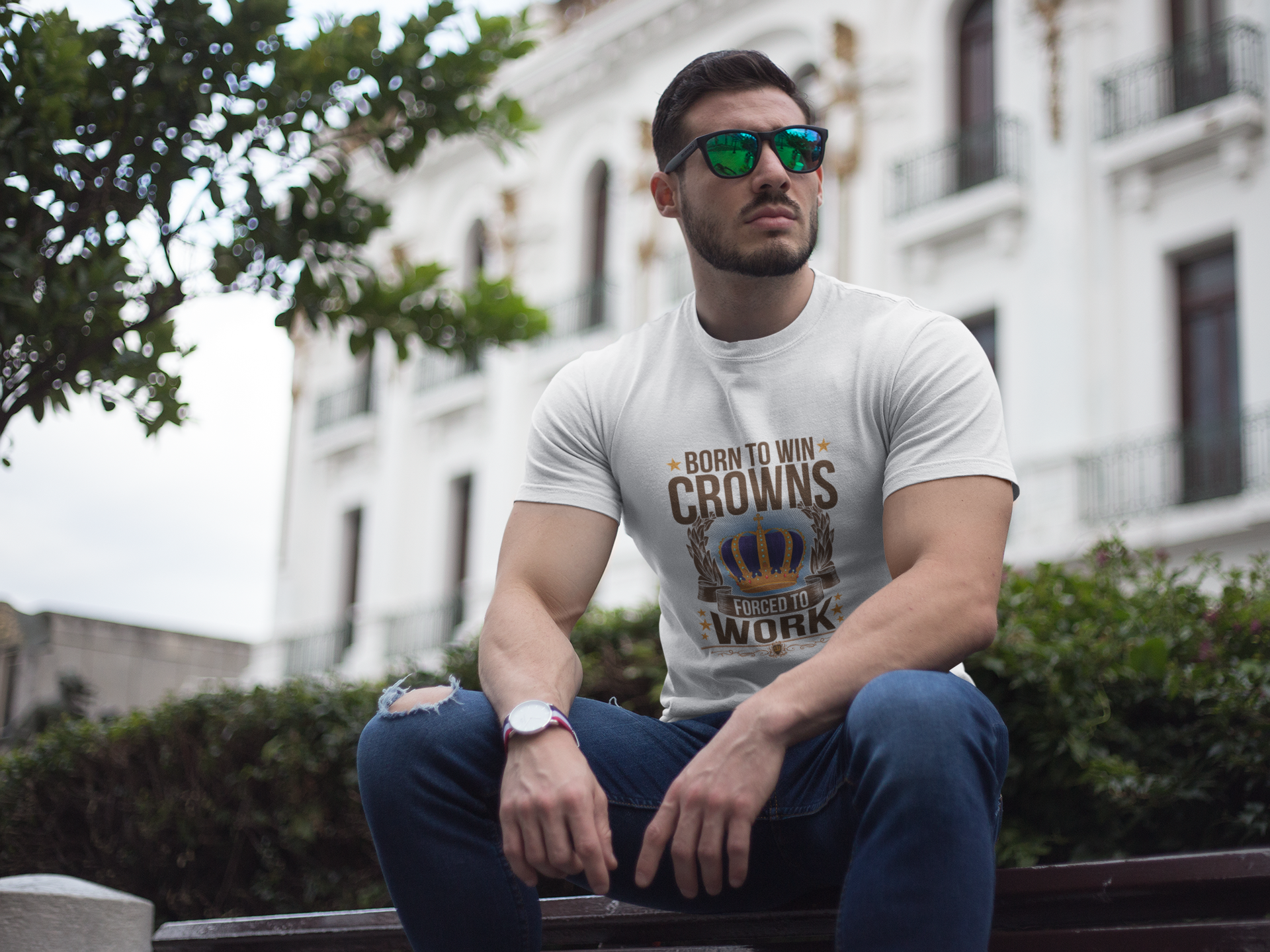 Man sitting on a bench wearing a t-shirt with text and sunglasses, with a building in the background.
