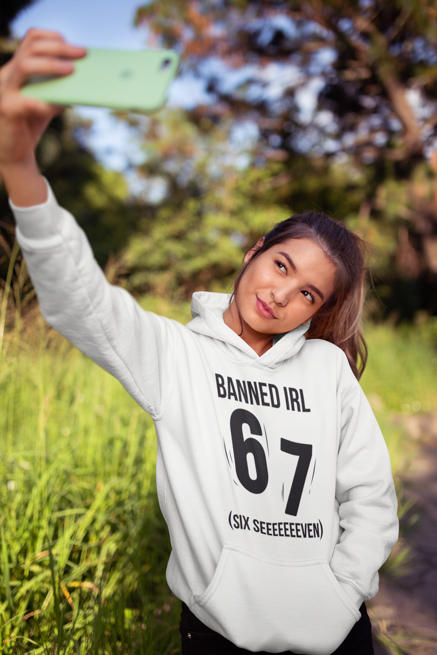 Person wearing a white hoodie with text, taking a selfie outdoors.