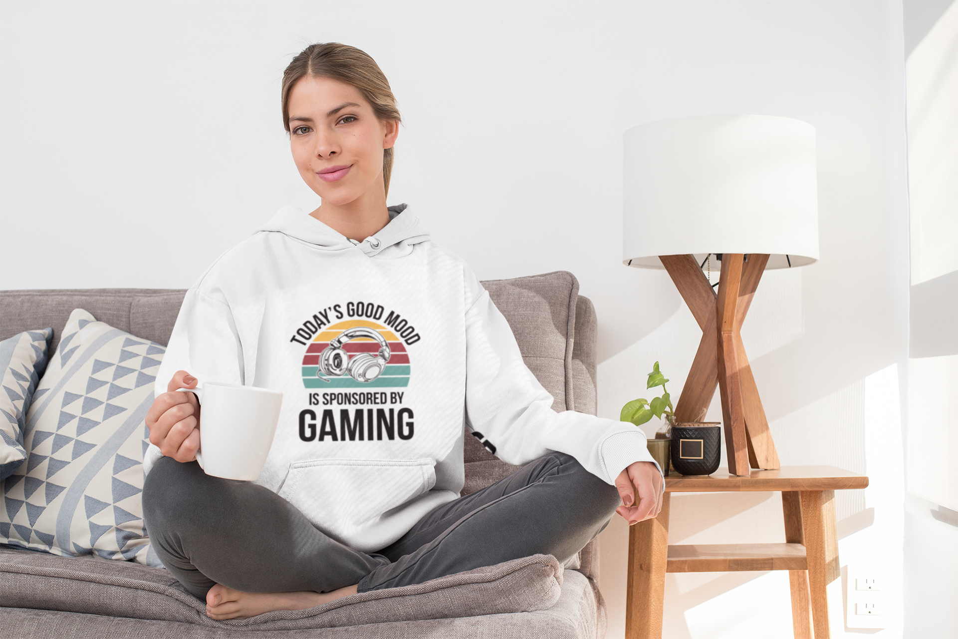 Woman wearing a hoodie with a gaming-themed design sitting on a couch in a living room.