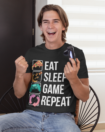 A smiling young man sitting in a chair wearing a black graphic T-shirt with the phrase 'EAT SLEEP GAME REPEAT' in white text and four colorful game controller icons. He is holding a smartphone in one hand and gesturing with the other.