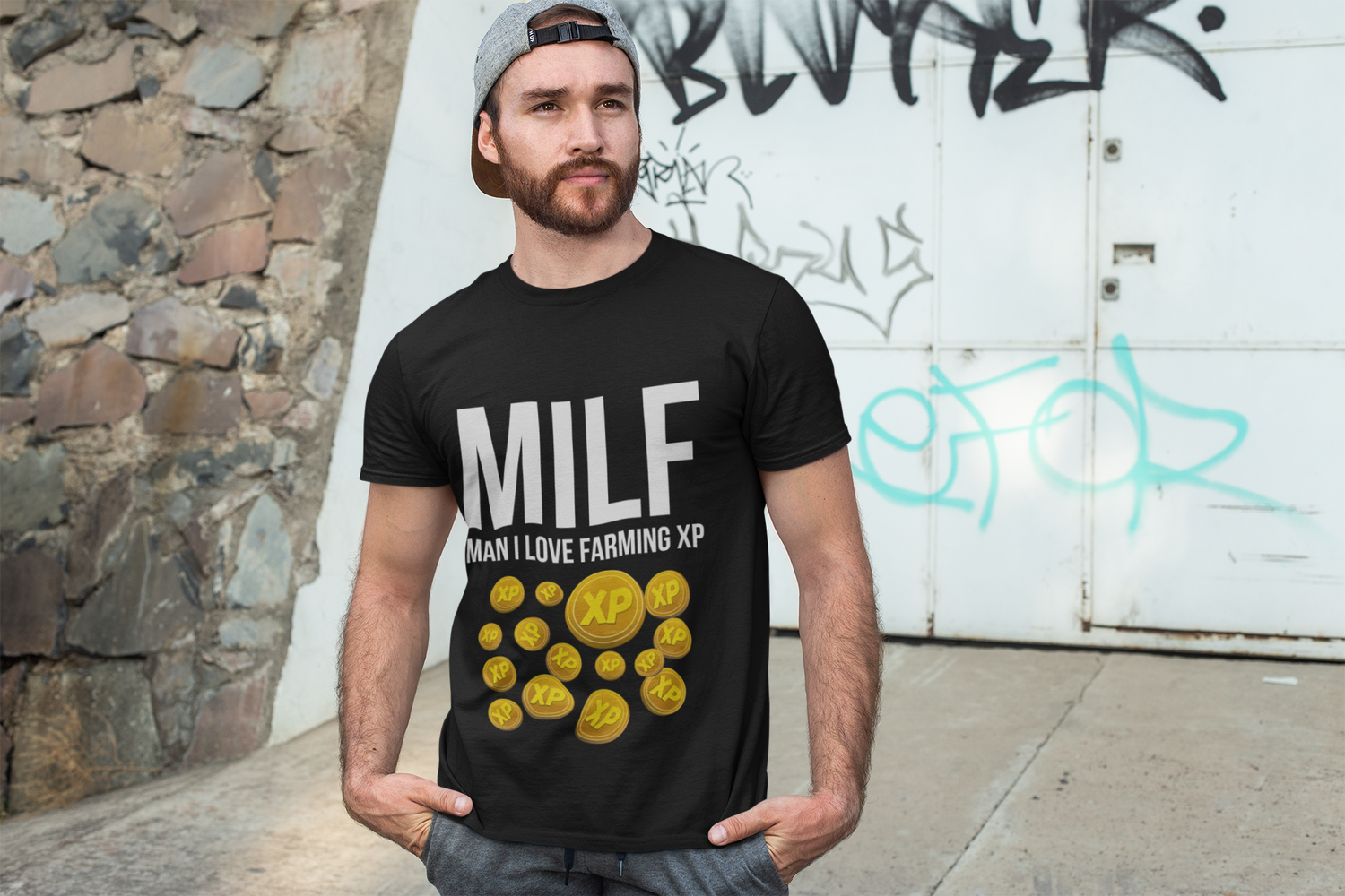 Man wearing a black t-shirt with graphic design and text, standing against a graffiti-covered wall.